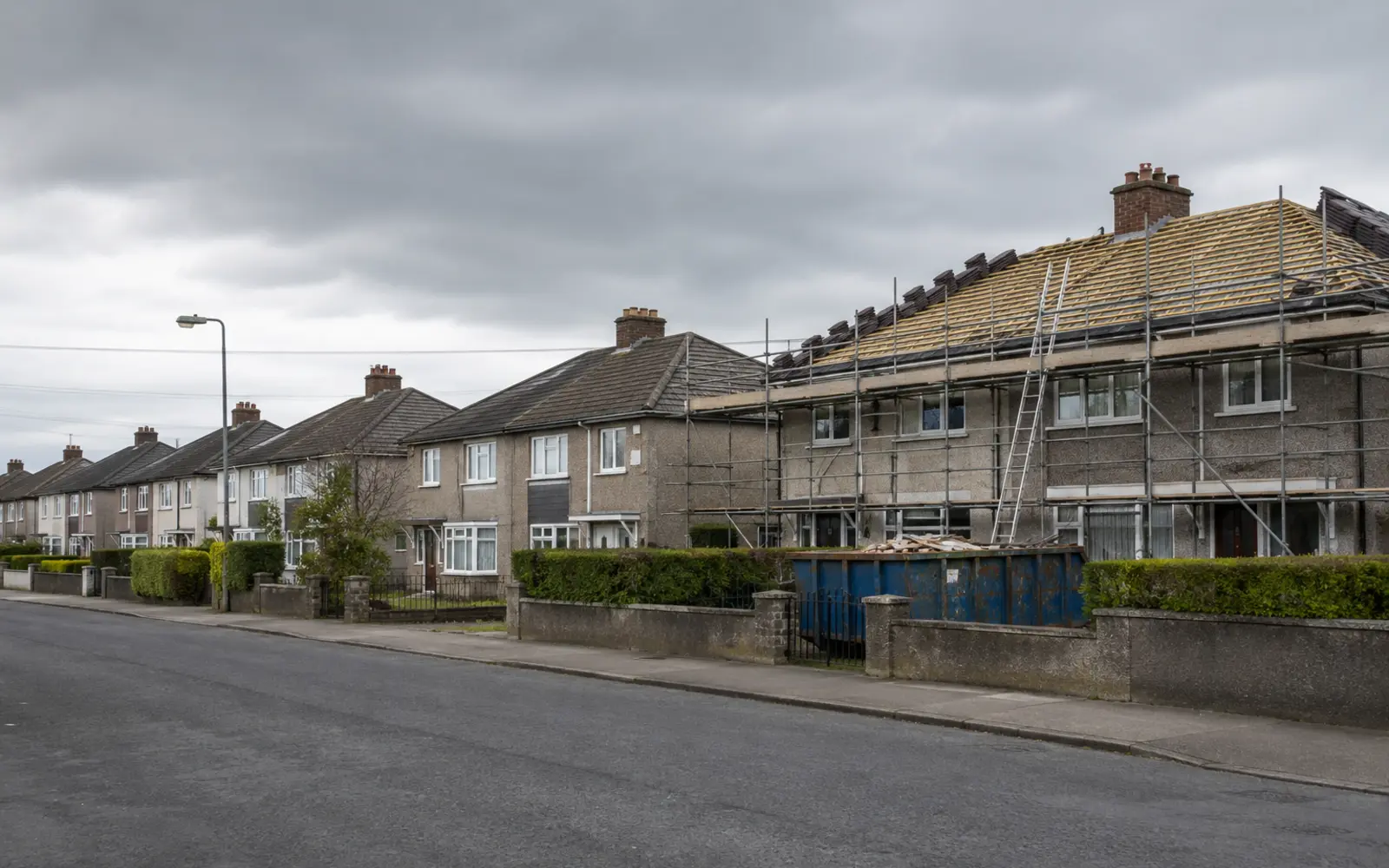 A row of suburban Dublin semis with one mid strip-and-reroof, scaffold and skip in place