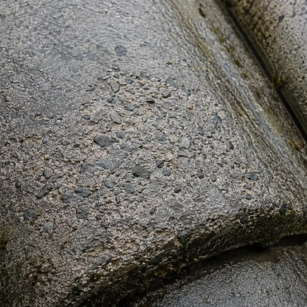 A concrete roof tile gone porous with aggregate showing through the worn face